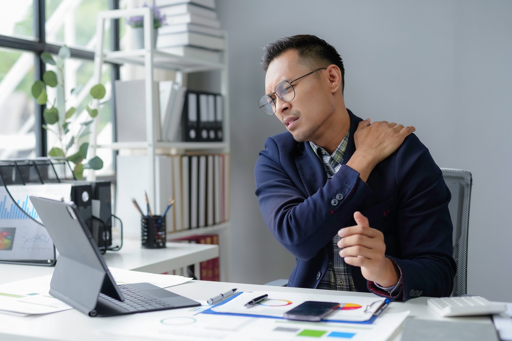 Asian businessman having shoulder and neck pain while working on a laptop