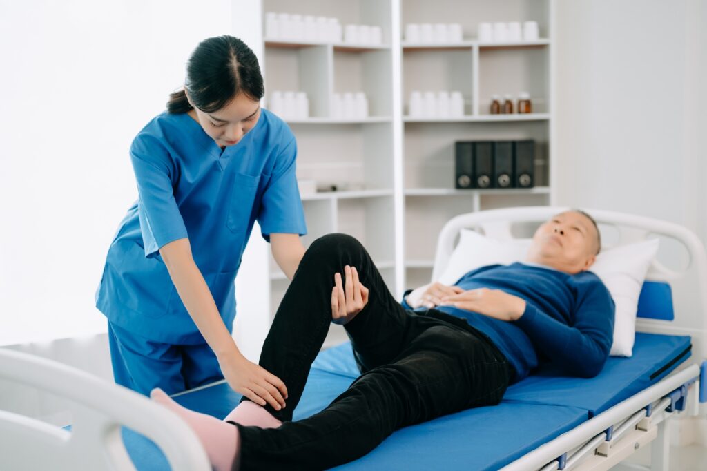 Physiotherapist Helping Patient While Stretching His Leg in bed in clinic